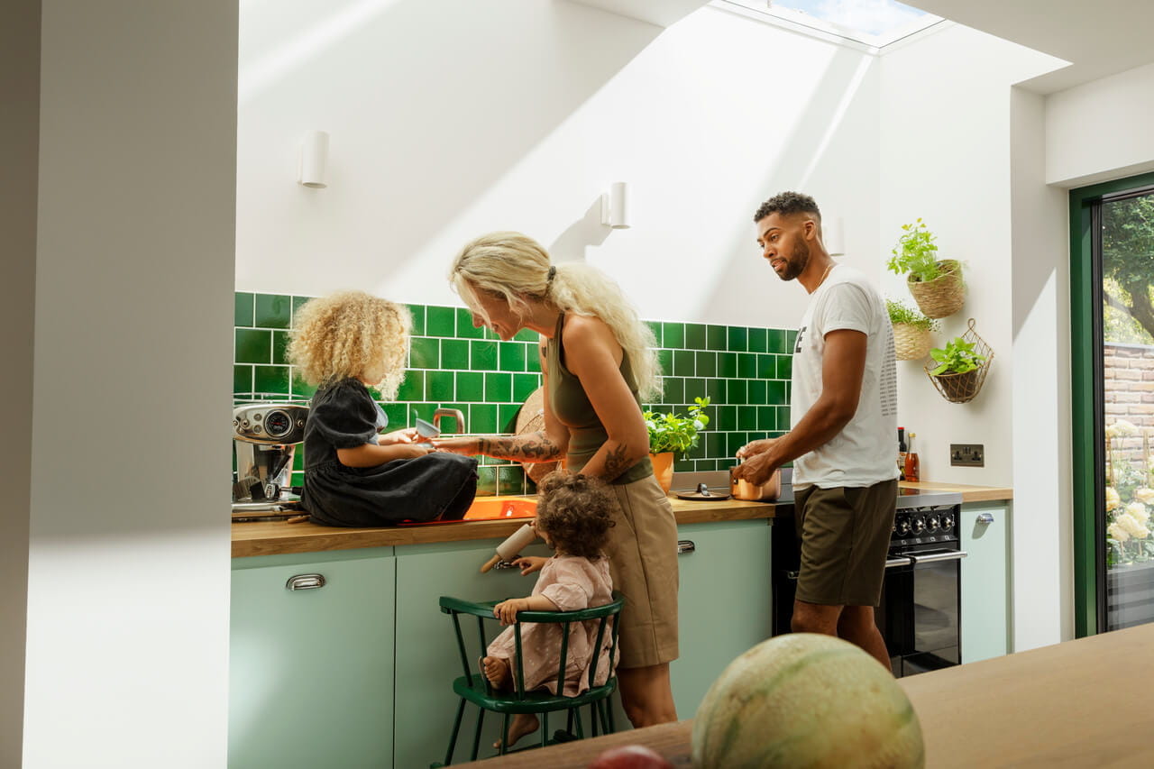 Family cooking in the green painted kitchen under a modern flat roof window