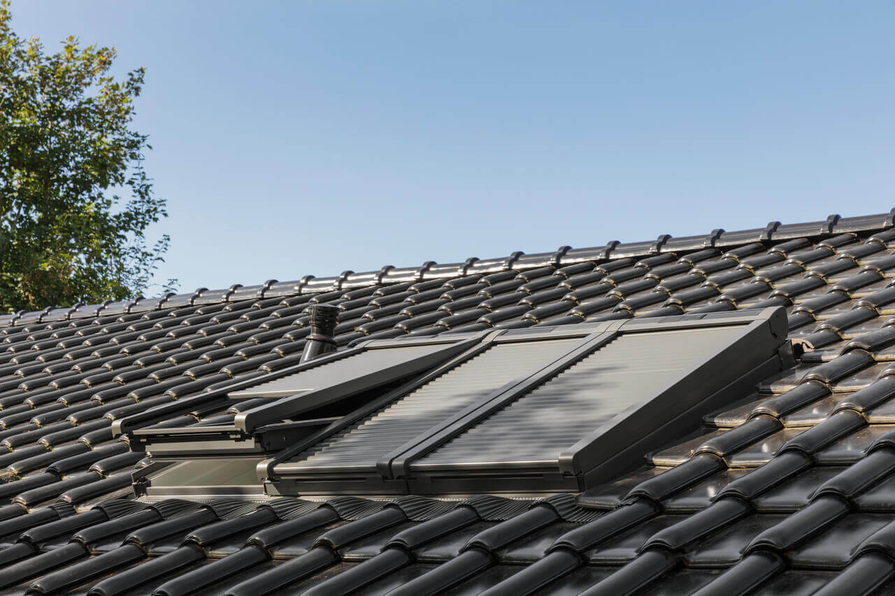 Exterior image of a black roof with 3 VELUX roller shutters installed, one partially opened.